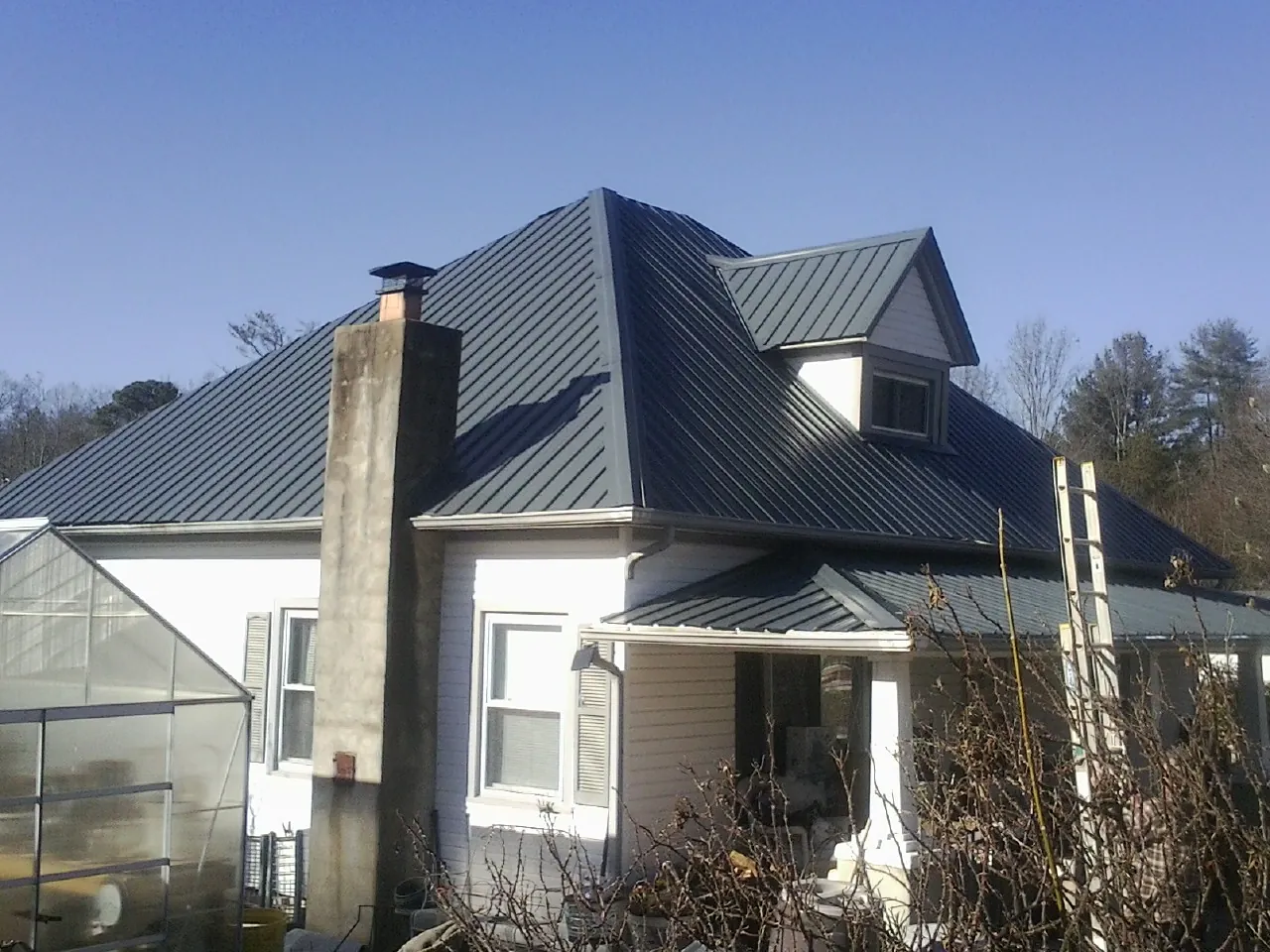 Dark blue standing seam metal roof on a white farmhouse with dormer — Slate & Tile Roof Repair by Roofing Brothers in New Troy