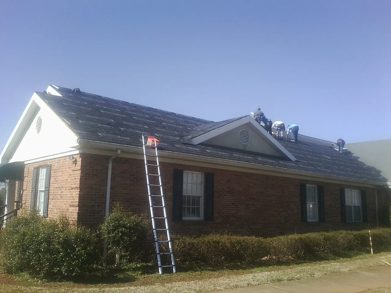 Crew tearing shingles off a brick ranch roof with a ladder set — Emergency Roof Repair work by our crew in New Troy
