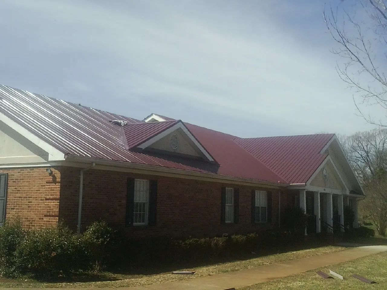Red metal roof with gabled entries on a long brick building, from a Hail Damage Roof Repair job in New Troy