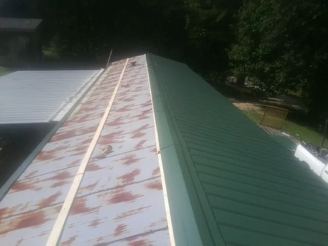 Old rusted panels beside newly installed green metal roofing — Wind Damage Roof Repair by Roofing Brothers in New Troy