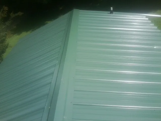 New green metal panels meeting at the ridge of a roof — Flat Roof Repair work by our crew in New Troy