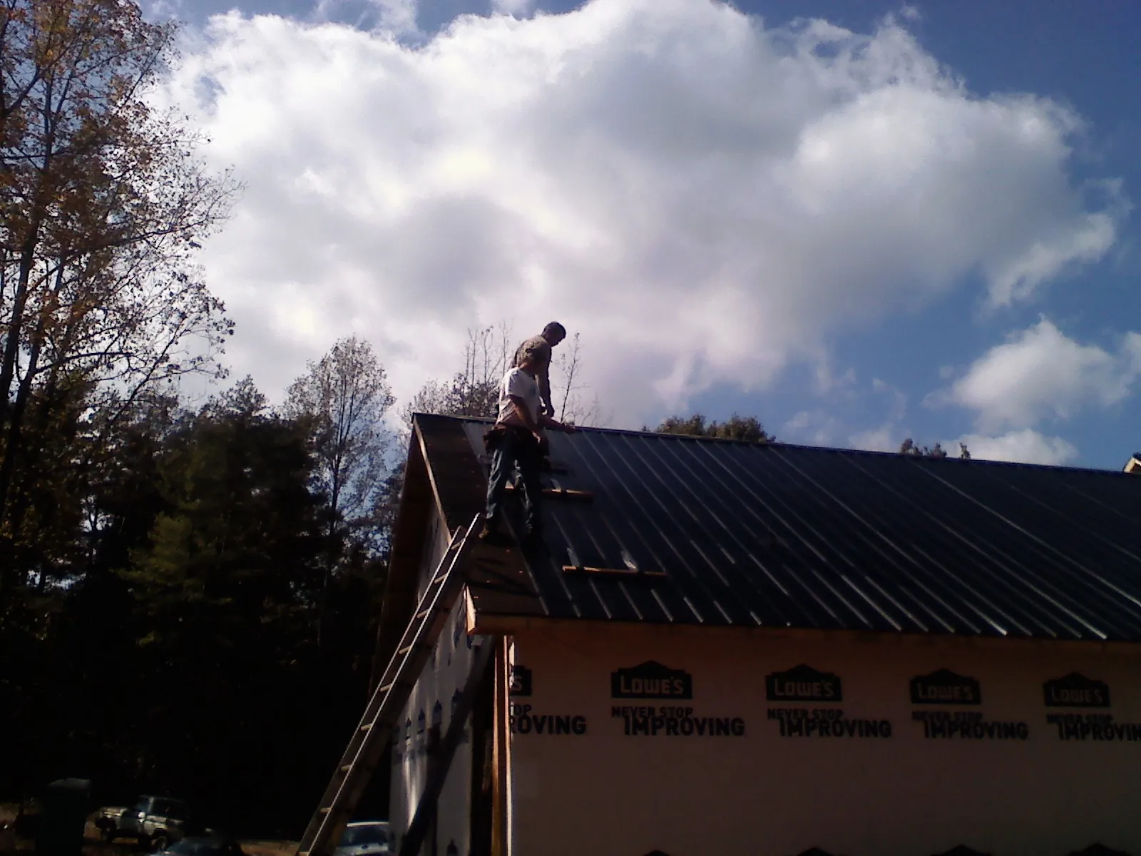 Roofer fastening dark metal panels high against a cloudy sky, from a Roof Inspection job in New Troy
