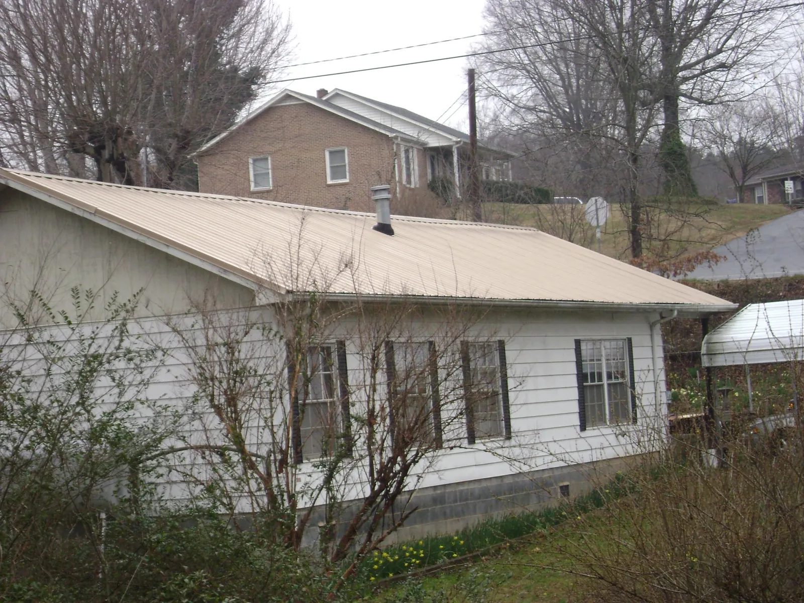 Tan metal roof on a white sided house set into a hillside — Commercial Roofing by Roofing Brothers in New Troy