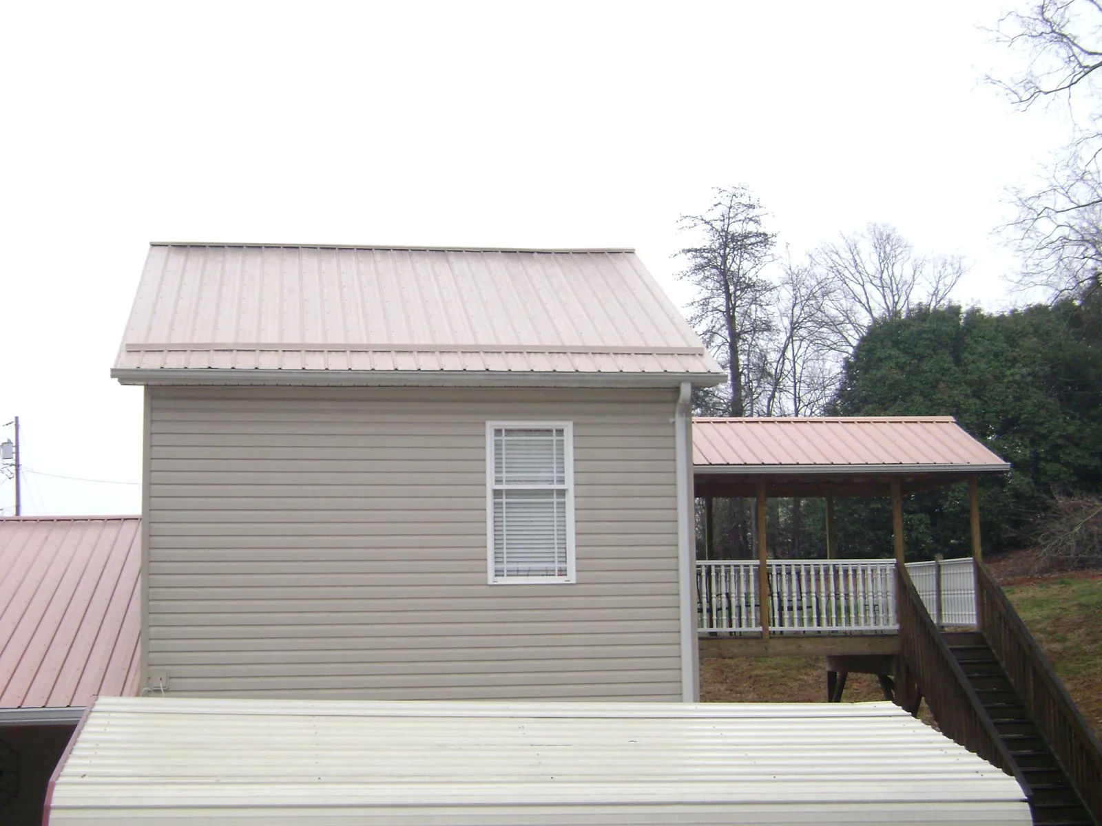 Tan metal roofs on a two story addition and attached porch, from a Roof Replacement job in New Troy